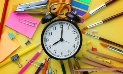 Photo of alarm clock against a backdrop of pens, rulers and paper signifying school start timesr