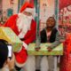 Photo of a young student sitting next to Santa Claus with a wrapped gift