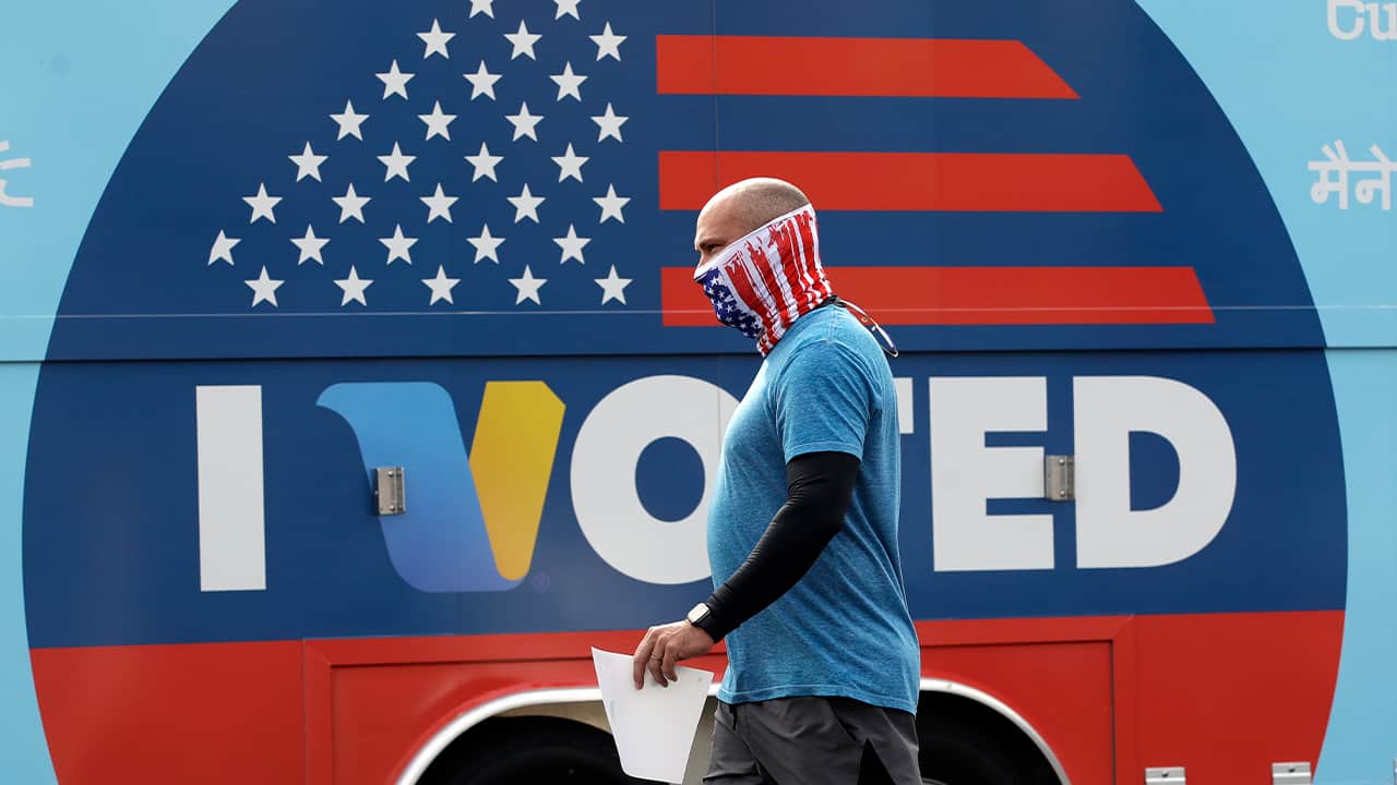 Photo of a man walking past an I Voted sign